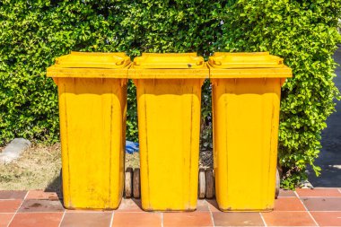 Yeşil yaprak arka plan üzerinde wate ayırma ve geri dönüşüm için sarı plastik çöp kutusu Satır