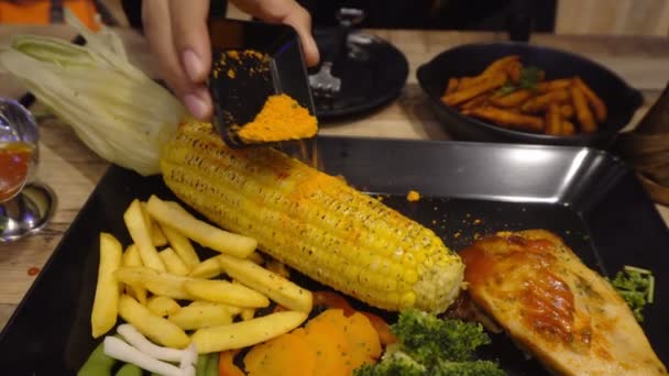 Hände Gießen Gewürze Auf Hühnersteak Mit Mais Und Kartoffeln Auf — Stockvideo