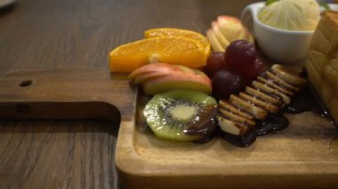 Ballı tost masanın üzerindeki ahşap tabakta elma, kivi, dondurma, portakal, üzüm ve çikolatayla birlikte..