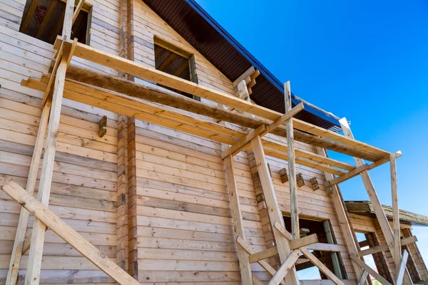 The house with a wooden structure is being built surrounded by scaffolding, blue sky