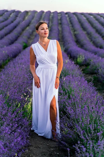 Beyaz elbiseli güzel bir kadın lavanta tarlasında poz veriyor. Aromaterapi, tarım, üretim kavramı. — Stok fotoğraf