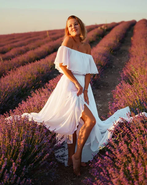 En vacker ung kvinna i vit klänning poserar på ett lavendelfält. Begreppet aromaterapi, jordbruk, produktion. — Stockfoto