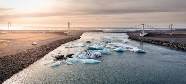 Chunks of ice scattered across a glacier lagoon in Iceland and a bridge crossing the image