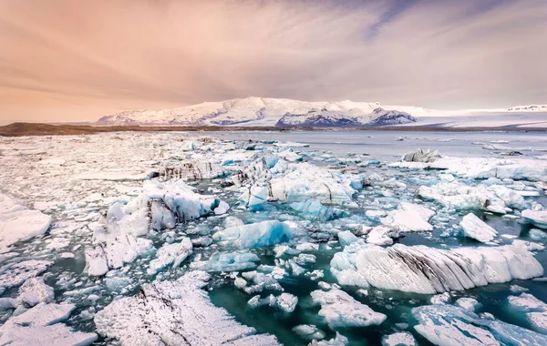 アイスランドの氷河のラグーンに散在する氷の塊で 背景に雪に覆われた山があります — ストック写真