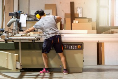 Marangoz kulak tıkacı takan bir makineyle odun kesiyor. Seçici odak