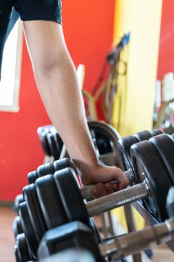 Spor salonunda elinde dambıl tutan genç adam.