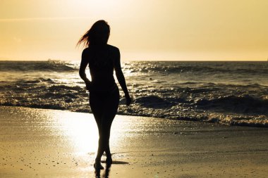 Sahilde gün batımında güzel bir kadının silueti.