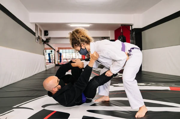 Man and woman training martial arts and judo with kimonos on the gym floor mat with a face mask because of the covid 19 coronavirus pandemic