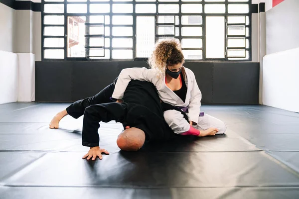 Man and woman training martial arts and judo with kimonos on the gym floor mat with a face mask because of the covid 19 coronavirus pandemic