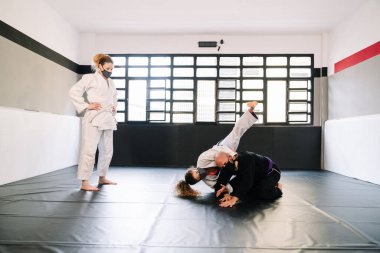 Judo ya da kimonolu karate gibi dövüş sanatları eğitiminin üç partneri spor minderinde pratik yapıyor. Hepsi de kovid 19 koronavirüs salgınından dolayı maske takıyor.