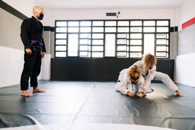 Judo ya da kimonoyla karate gibi bir dövüş sanatları eğitiminde üç ortak. İki kadın spor salonunun paspasında pratik yapıyor. Hepsi kovid 19 koronavirüs salgınından dolayı maske takıyor.