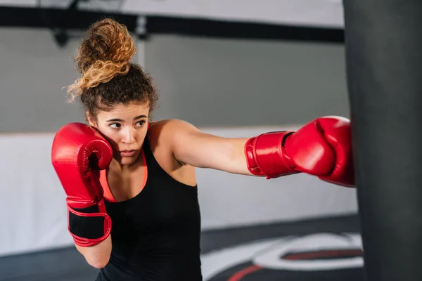woman boxer training very concentrated with red boxing gloves punching directly into a punching bag in a gym