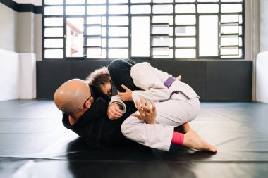 Erkek ve kadın dövüş sanatları eğitimi veriyor ve spor salonunun zemininde kimonolarla judo yapıyor. Yüz maskesi takıyorlar. Çünkü kovid 19 koronavirüs salgını var.