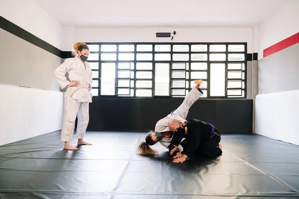 Three partners in a martial arts training such as judo or karate with kimonos practicing techniques on the gym mat all wearing face masks due to the covid 19 coronavirus pandemic