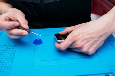 Teknisyen mavi çalışma yerindeki bir telefonu tamir ediyor..