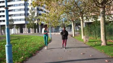 Kadın sporcular, doğal arka plana sahip kentsel park ortamında dinamik açık hava antrenmanı sırasında birbirlerini destekleyerek fitness antrenmanlarını senkronize ediyorlar.