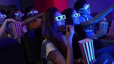 Üç boyutlu renkli gözlük takan genç arkadaşlar film gecesinde patlamış mısır paylaşıyorlar, yavaş çekim montajı yoluyla sinematik heyecan yaşıyorlar.