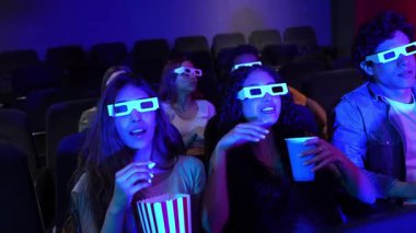 3 boyutlu gözlük takan gençler film izliyor, patlamış mısır yiyor, soda içiyor, birlikte vakit geçiriyorlar.