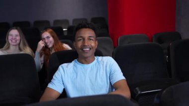 Genç bir adamın sinemada eğlenirken, filme gülüp tepki verirken, iki kızın arkasından fısıldadığı yavaş çekim videosu.
