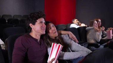 Genç çift samimi film anlarını paylaşıyor, loş aydınlatılmış sinemada birlikte patlamış mısırın tadını çıkarıyorlar. Yavaş çekim sinematografisi ile.