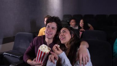 Genç çift film gecesi mahrem bir anı paylaşıyor, patlamış mısırın tadını çıkarıyor ve sinema salonunda hafif ışıklandırmada sevgi dolu bir bağ kuruyor.