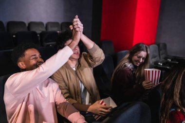 Karanlık bir tiyatroda birlikte kutlama yapan, beşlik çakan, patlamış mısırın keyfini çıkaran ve film izlerken gülen bir grup genç öğrenci.