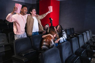 Heyecanlı gençler tezahürat yapıyor, sarılıyorlar, spor zaferinin tadını çıkarıyorlar, ellerinde patlamış mısır kovalarıyla sinemada.