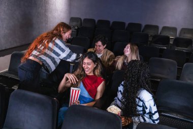 Bir grup arkadaş birlikte gülerken sinemada eğlenceli bir film izliyorlar, patlamış mısır paylaşıyorlar ve neşeli anılar yaratıyorlar.