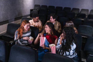 Genç insanlar sıcak bir sinemada heyecan verici bir film izlerken gülüyor ve patlamış mısırdan zevk alıyorlar, neşe ve beraberlik anlarını paylaşıyorlar.