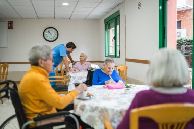 Parlak ortak alandaki bir masada yaşlı kadınları kontrol eden sağlık uzmanı, destek ve bakım sunar.