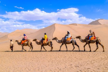 Turist grubu kum dağı Mingsha Shan çölünde deveye biniyor ya da Çin 'in Gansu kentindeki Dunhuang şehrinde İpek Yolu' nun bir parçası olarak kervanla şarkı söyleyen kum tepelerinde..