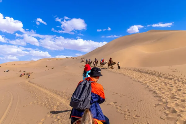 Group of tourists are riding camel at the sand mountain Mingsha Shan desert or the singing sand dunes with the caravan as part of the Silk Road in Dunhuang, Gansu, China.
