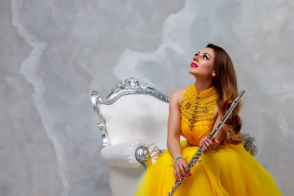 Female in yellow dress with flute on white background. Flute in hand. Stylish girl with musical instrument (flute). Photo for magazine cover, website with space for an inscription or logo