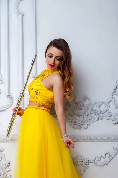 Woman in yellow dress with flute on light textured background. Flute in hand. Stylish girl with musical instrument (flute). Photo for magazine cover, website with space for an inscription or logo