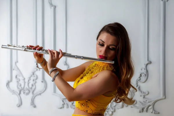 Woman in yellow dress with flute on light textured background. Flute in hand. Stylish girl with musical instrument (flute). Photo for magazine cover, website with space for an inscription or logo