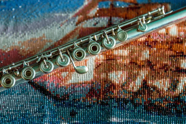 Flute on bright colored background of beads. Part of silver flute lies on blue background. Space for your creativity, creating an inscription or logo. Concept of musical work or concert