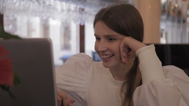 傍晚时分 穿着白色夹克的斯拉维茨姑娘身穿手提电脑坐在吧台桌旁 流露出她的情感 女人的微笑在网上交流 接电话 年轻女子的特写 — 图库视频影像
