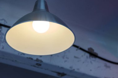 Tavanda gölgede bir lamba. Eski püskü arka planda aydınlatma cihazı. Tavanın altında büyük bir gölge var. Modern elektrik avizesini asıyorum. Etiketiniz veya logonuz için boşluk içeren yatay fotoğraf