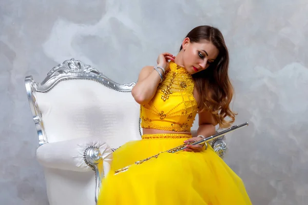 Female in yellow dress with flute on white background. Flute in hand. Stylish girl with musical instrument. For magazine cover, website. Author's space. Large background space for inscription or logo
