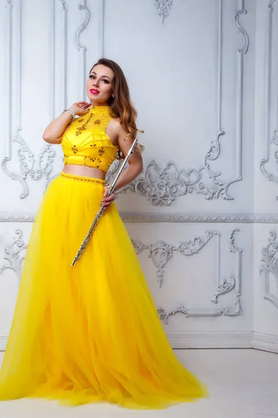 Female in yellow dress with flute on white background. Flute in hand. Stylish girl with musical instrument. For magazine cover, website. Author's space. Large background space for inscription or logo