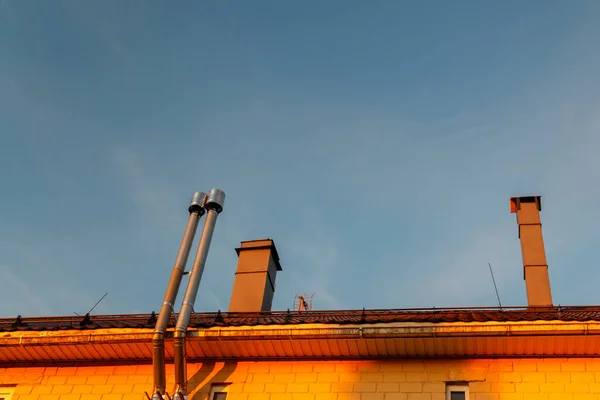 Roof of house with chimneys against clear blue sky. Modern metal roof with iron chimneys. Iron pipe on roof of house. Bottom view, author\'s space. Large background space for an inscription or logo