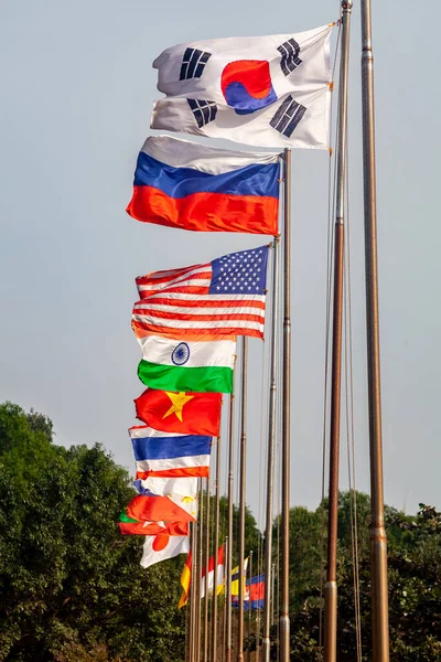 Flags different countries on high flagpoles. National flag different fluttering in wind. Flag Korea, Russia, United States, India, Vietnam, Cambodia and other against blue sky. Natural vertical photo