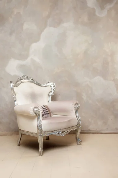 An antique white chair against wall. Antique leather chair. There is striped pillow on chair
