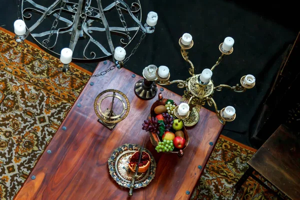 Table with fruits and vegetables in medieval room with chandeliers and candles. View from top. Style of old feasts with silver dishes, fruit. Copyright space. Large space for an inscription or logo