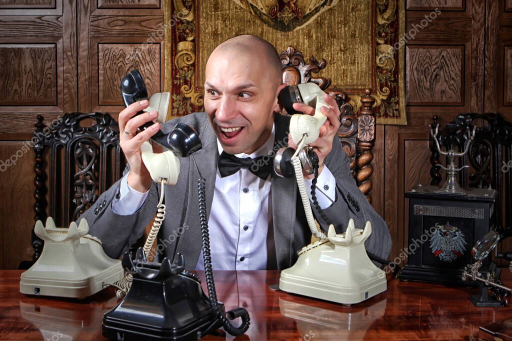 Fast-paced desperate businessman showman works in office and many calls, he keeps lot handsets. Business management concept. Stressed man talks on many phones at once. Space for inscription or logo