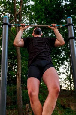 Karantina sırasındaki spor, kentsel koşullarda kendini izole etme. Genç bir adam, sporcu bardan çekiyor. Siyah tıbbi maske takıyor. Covid-19 koronavirüs salgını. Aktif bir insanın hayatı