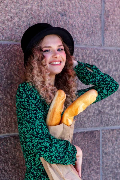 Portrait woman dressed in French style with baguette in hand. French style of Paris. Close-up of French woman in stylish clothes holding fresh baguettes and smiling. Place for an inscription or logo
