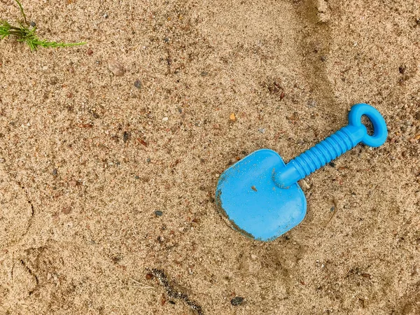 Child\'s shoulder blade on wet sand. Blue blade in sand on beach. Abandoned, forgotten toy shovel. Concept summer children\'s recreation after quarantine. Texture sand. Place for an inscription or logo