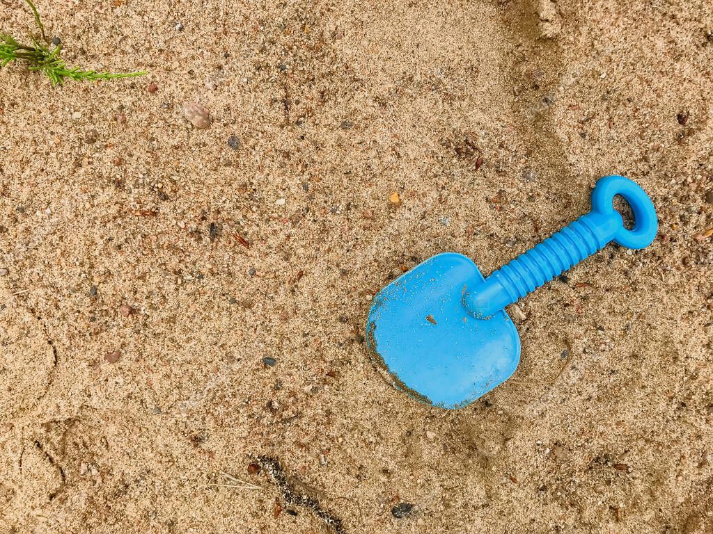 Child's shoulder blade on wet sand. Blue blade in sand on beach. Abandoned, forgotten toy shovel. Concept summer children's recreation after quarantine. Texture sand. Place for an inscription or logo