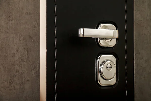 Metal door handle and door lock. Use your keys to lock black textured door. Keyhole and doorknob close-up. Grey and black door with chrome handle and keyhole. Space for your text or logo